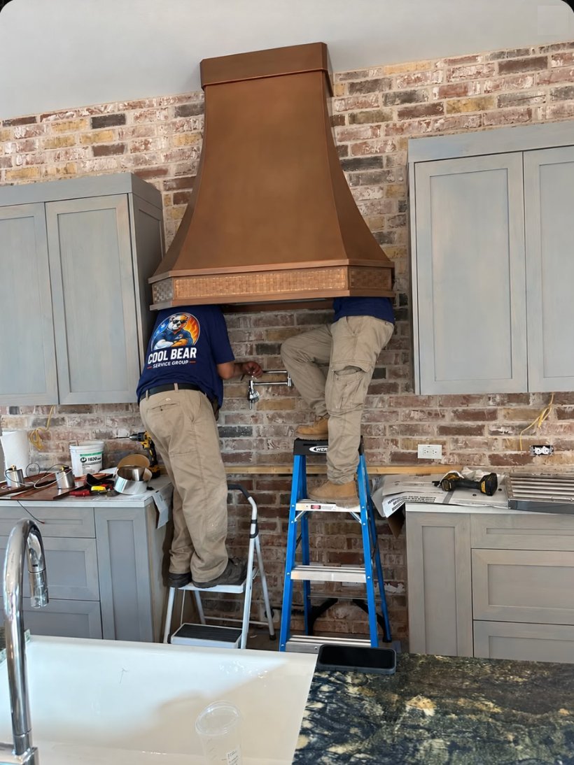 Cool Bear Service Group technicians installing a custom copper vent hood over a brick kitchen wall