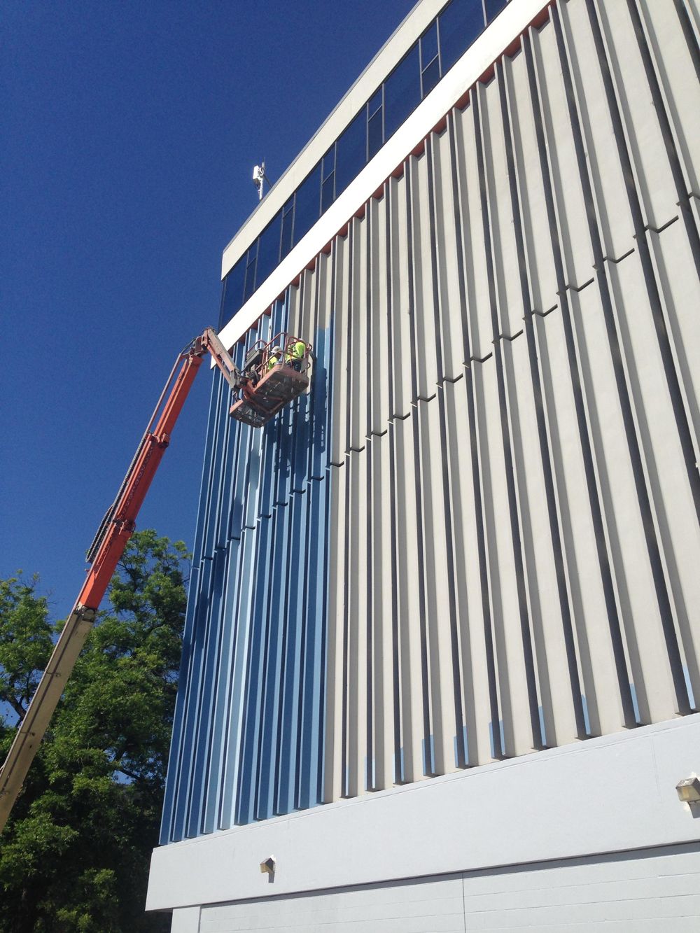 Boom lift crew painting blue fins on a commercial building exterior