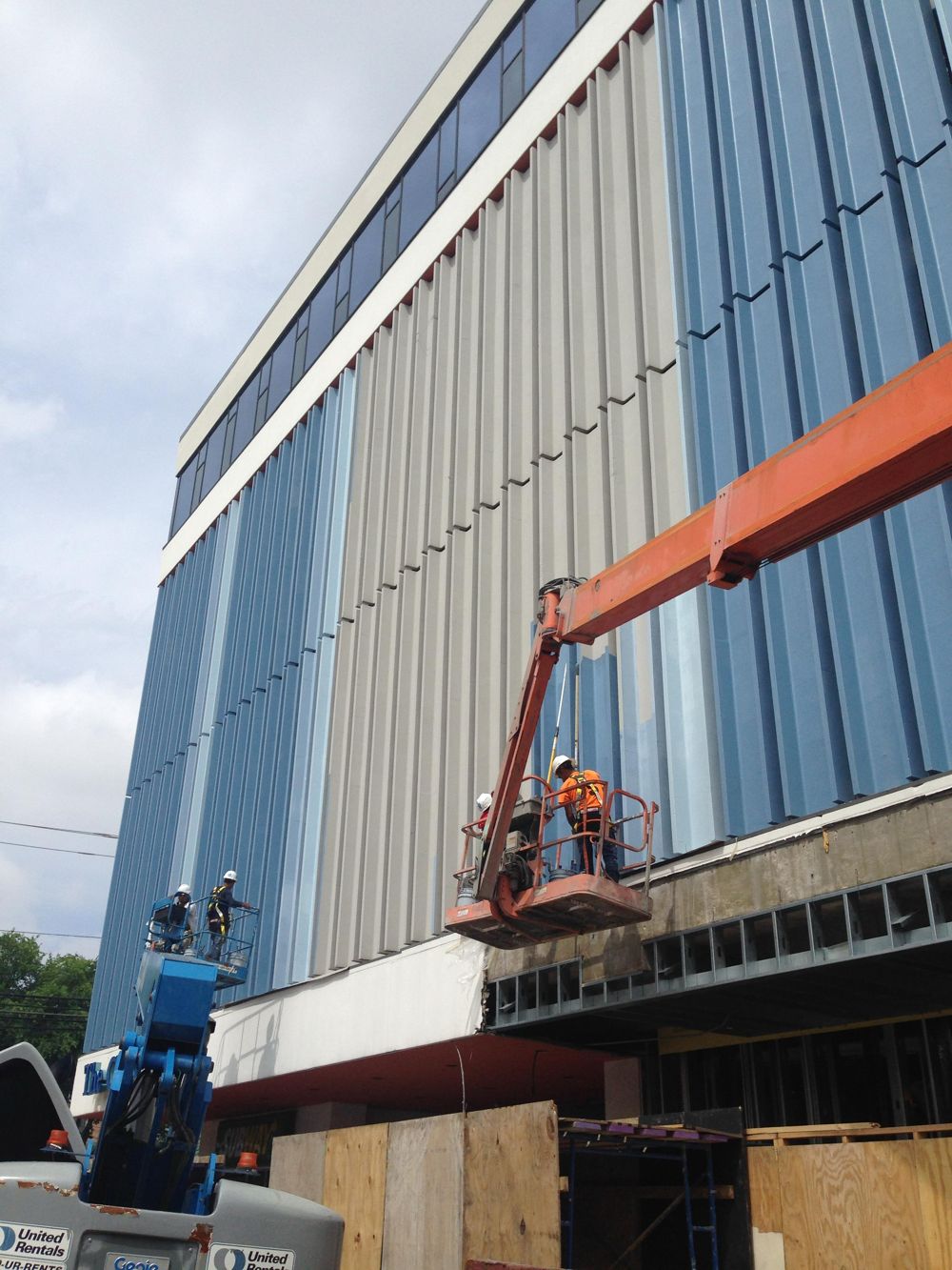 Crew on boom lifts repainting the vertical fins of a commercial building facade