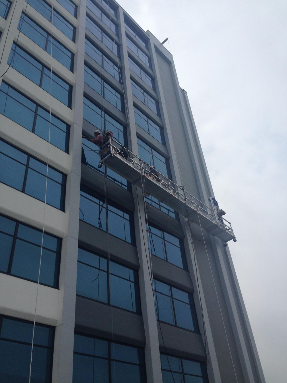 Worker on a swing stage working on the windows and panels of a tall commercial building