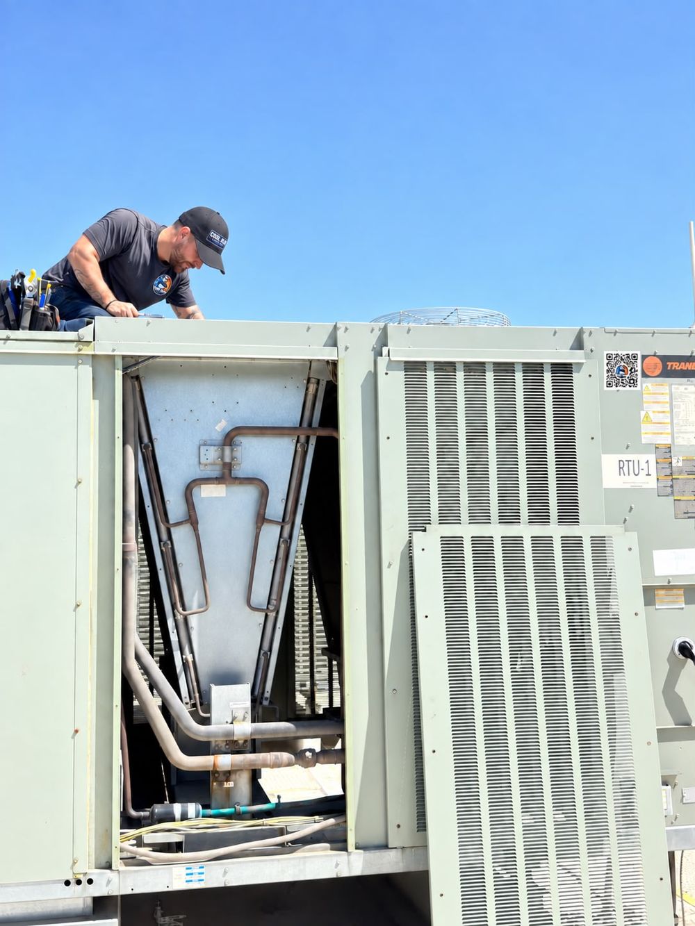 Cool Bear technician working on an opened Trane rooftop unit labeled RTU-1